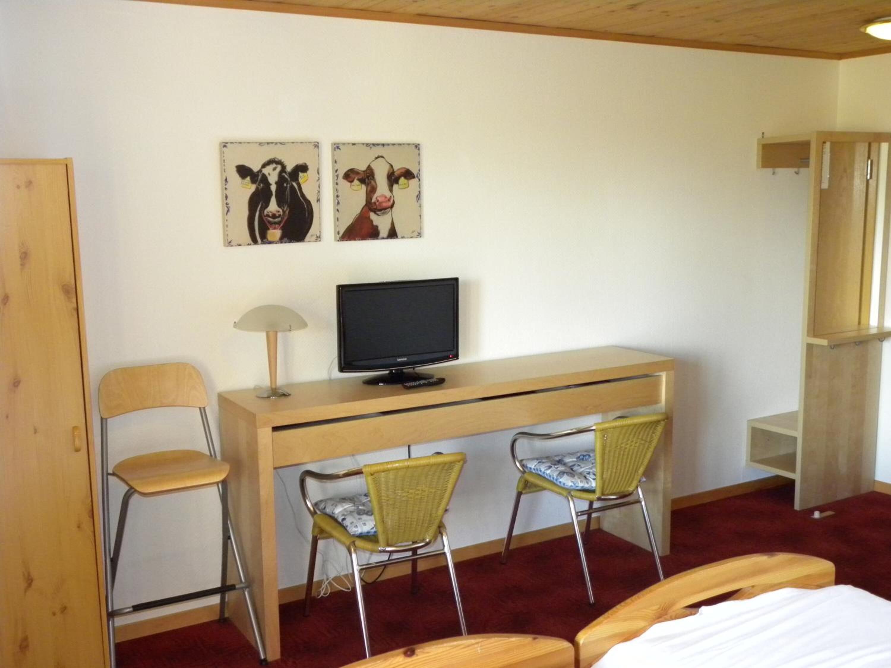 A room with a wooden desk, two chairs, a television, and artwork on the wall.