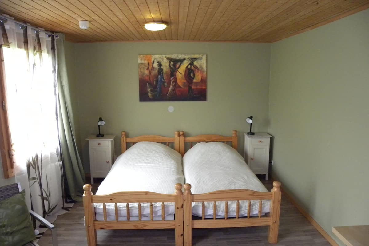 A room with a wooden bed, two bedside tables, a painting on the wall, and a window with curtains.