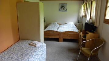 A room with two wooden beds, a chair, a desk with a computer, and a small wall-mounted shelf.