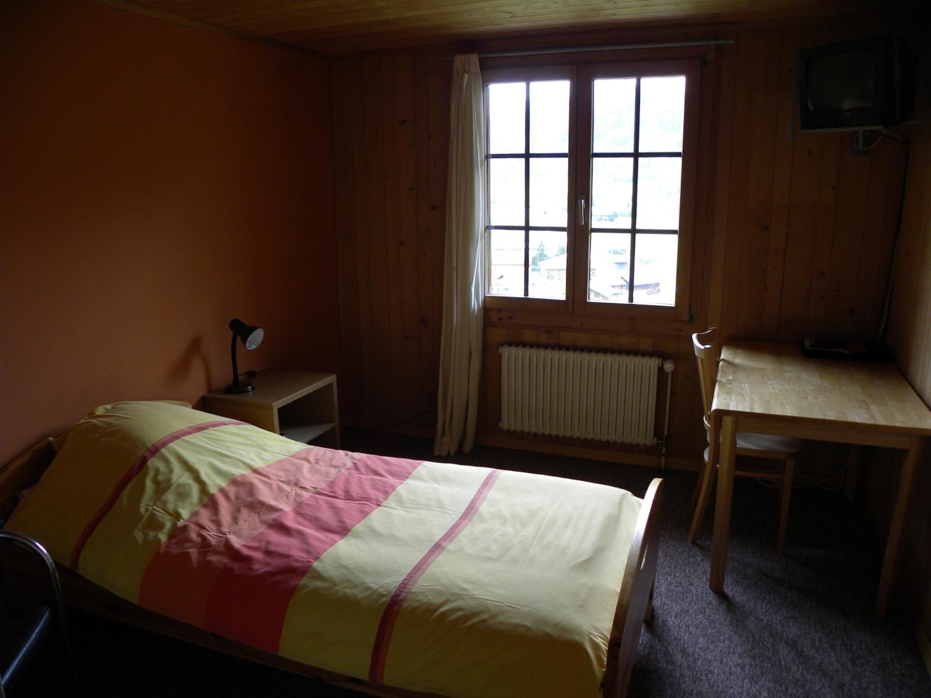 A room with a bed, a desk, a chair, a radiator, and a window.