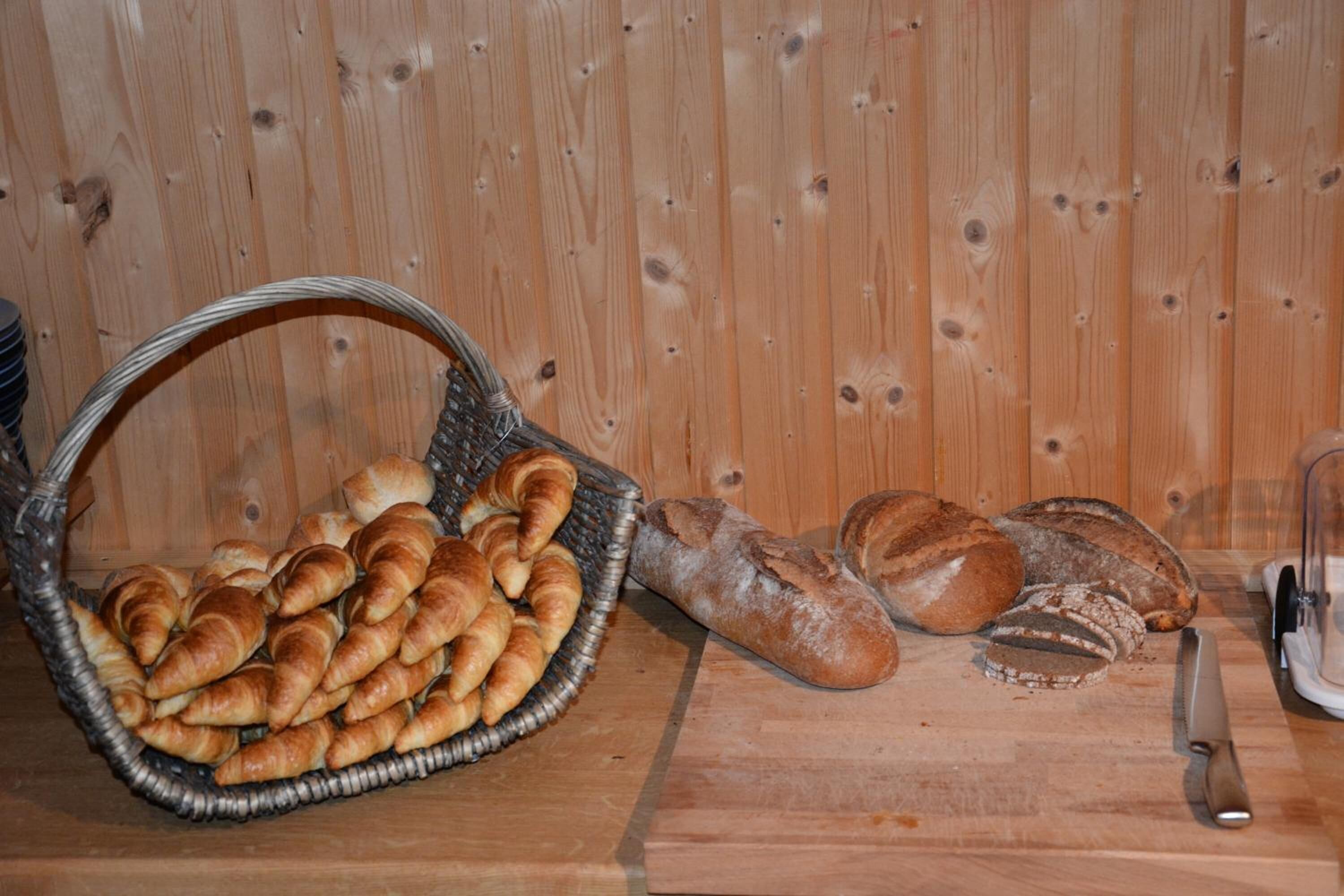 Una pared de madera con una cesta de croissants y una hogaza de pan sobre una mesa de madera.