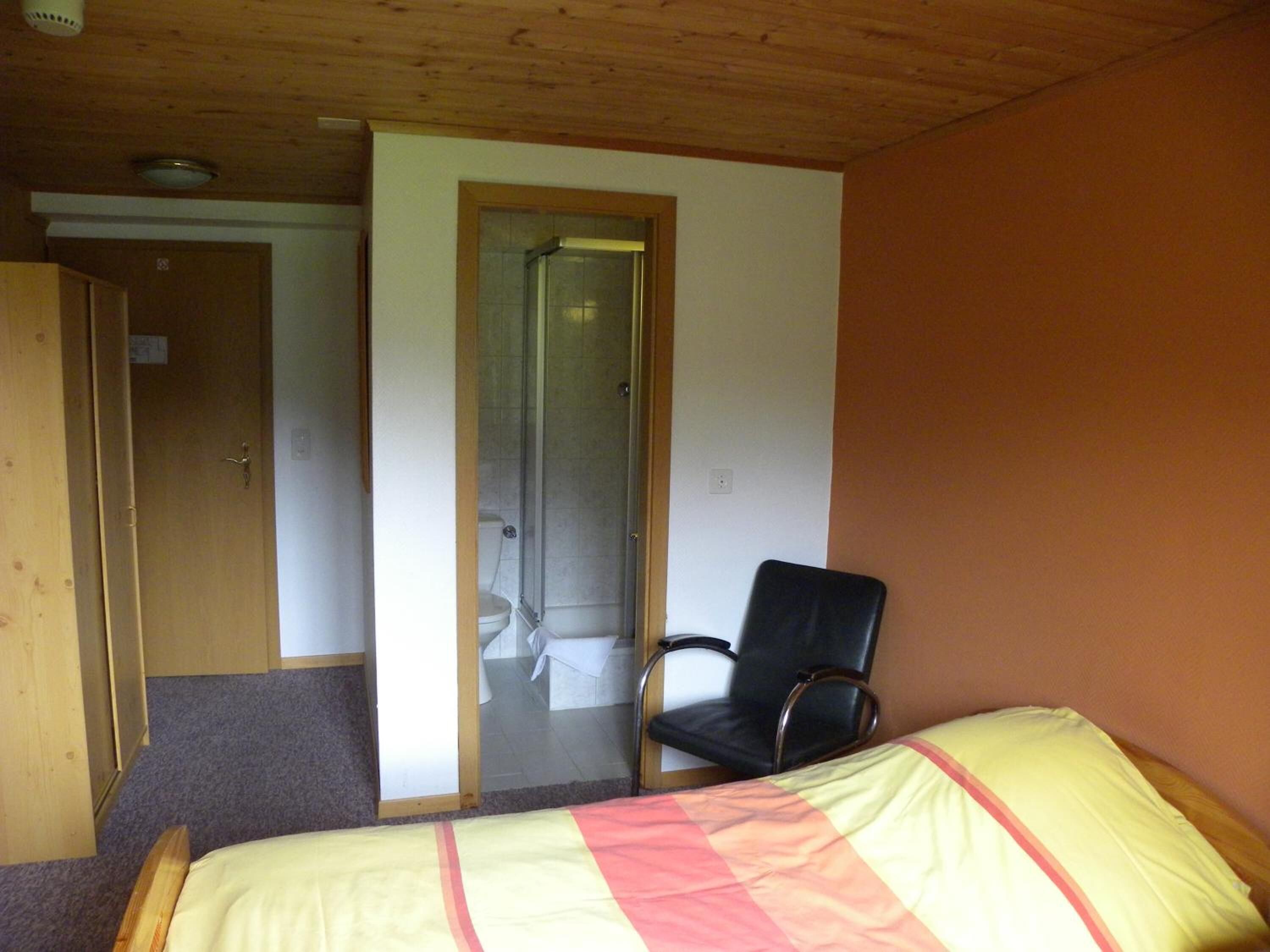 A bedroom with a bed, a chair, a shower, and a door.