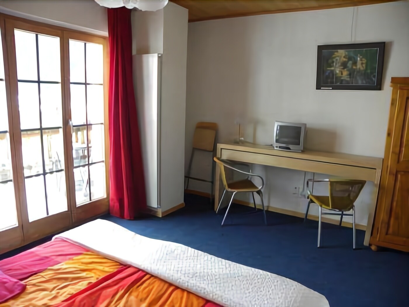 A bedroom with a bed, a desk, two chairs, a television, and a window with curtains.