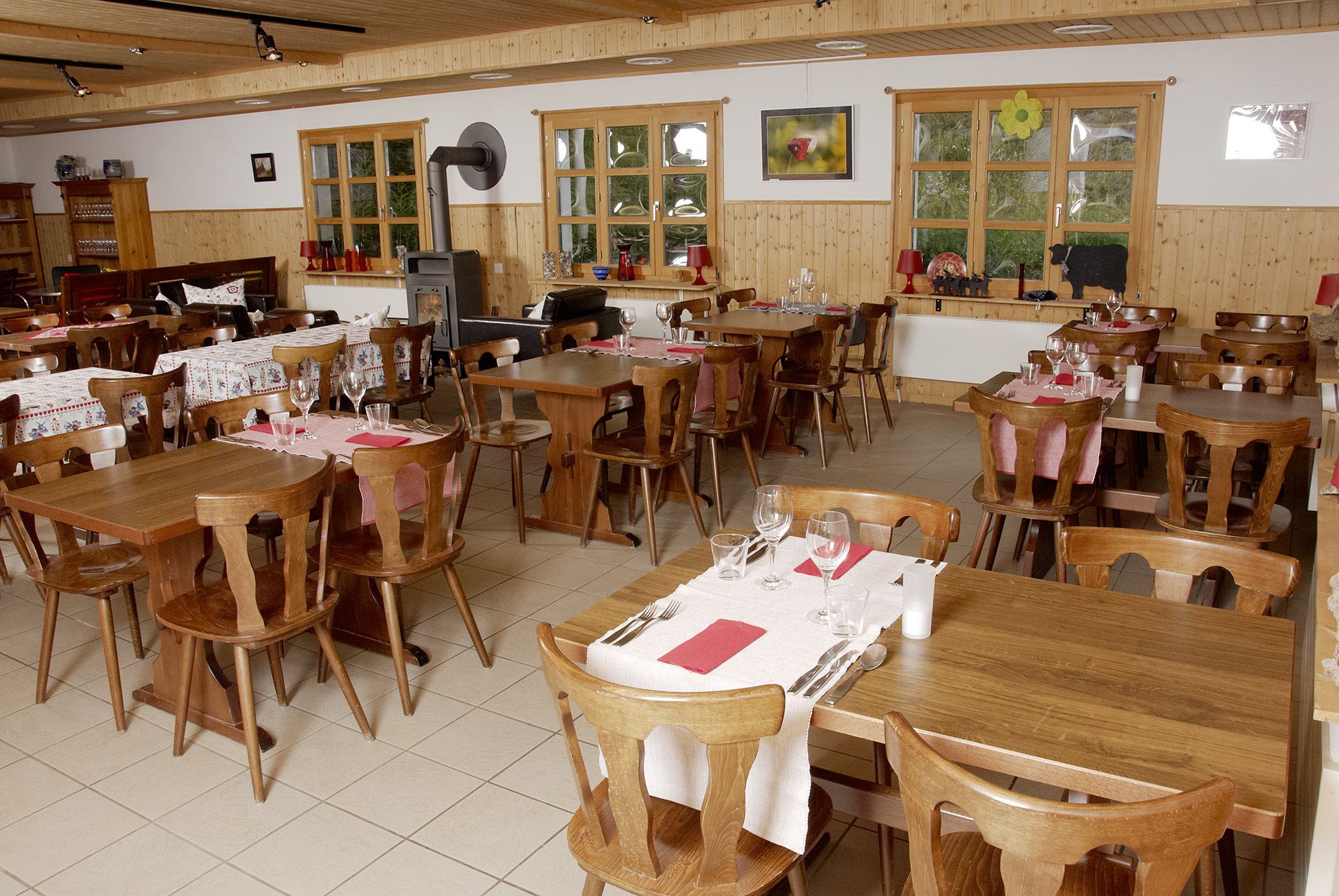 A dining area with wooden tables and chairs, a central fireplace, and large windows with flower decorations.
