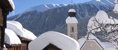 A snow-covered village with traditional wooden houses and a church with a clock tower.