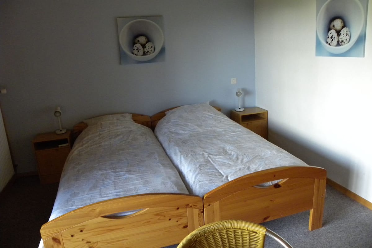 A bedroom with two single beds, wooden headboards, bedside tables with lamps, and wall-mounted picture frames.