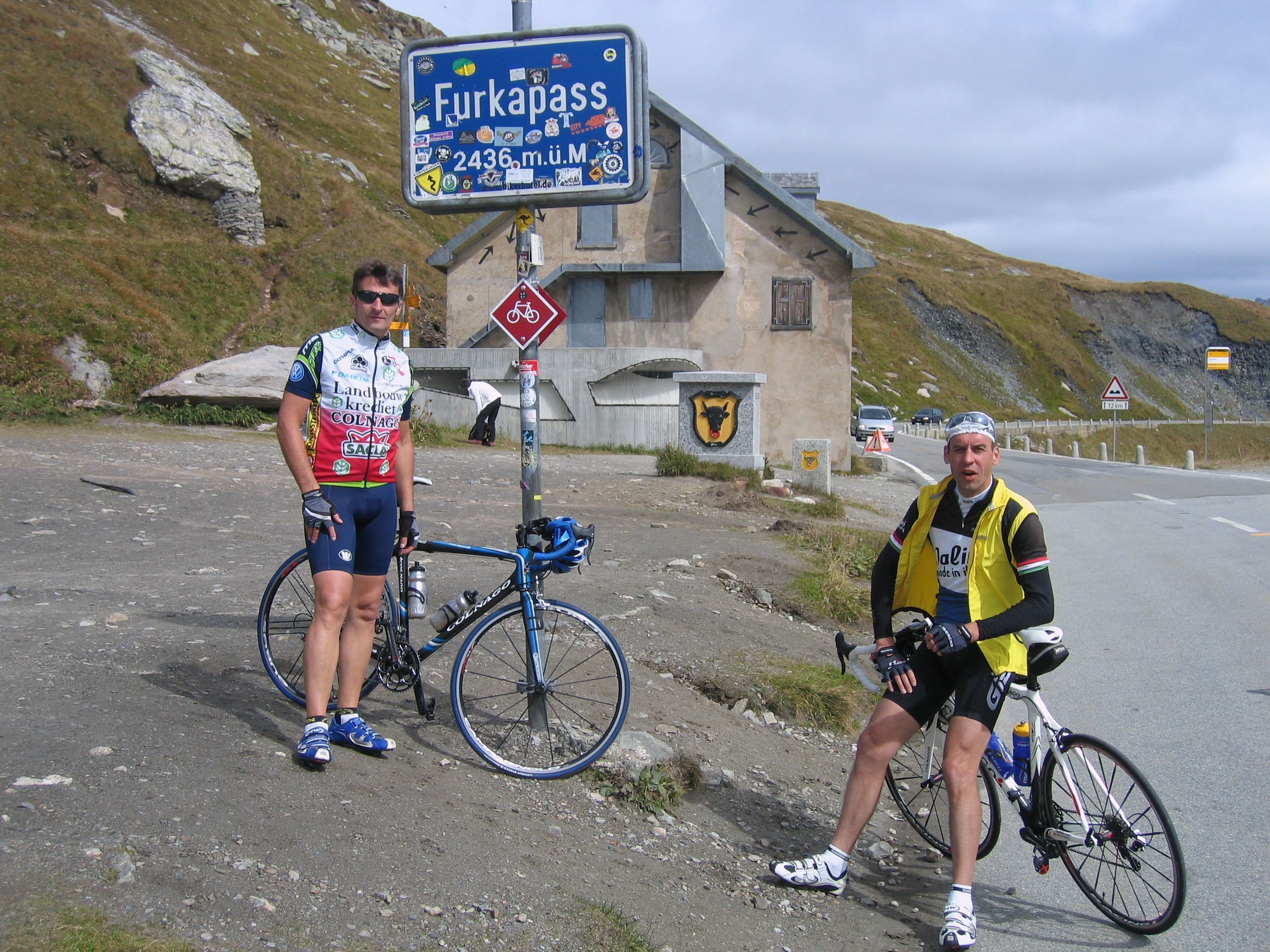 Dois ciclistas perto de um sinalizador com montanhas ao fundo.