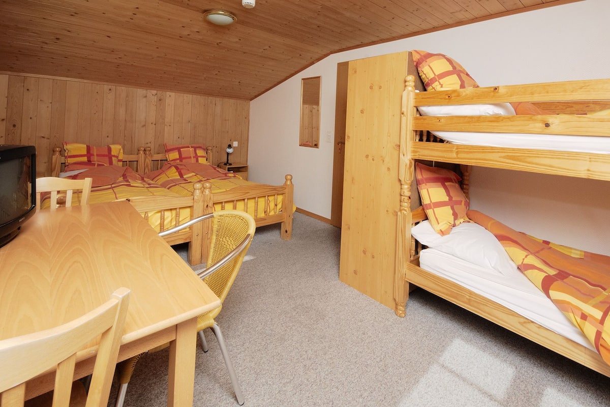 A room with bunk beds, a wooden table, chairs, and a television.
