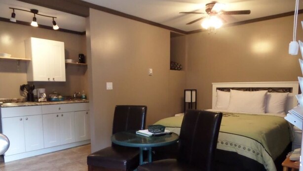 A compact hotel room with a kitchenette, a dining area with a table and chairs, and a bed with a green bedspread. - Riverside Motel (Port Alberni)