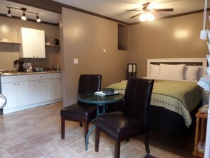 A compact hotel room with a kitchenette, a dining area with a table and chairs, and a bed with a green bedspread. - Riverside Motel (Port Alberni)