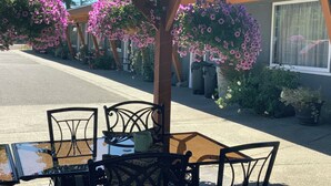 An outdoor seating area with metal chairs and a table, surrounded by hanging flower baskets. - Riverside Motel (Port Alberni)