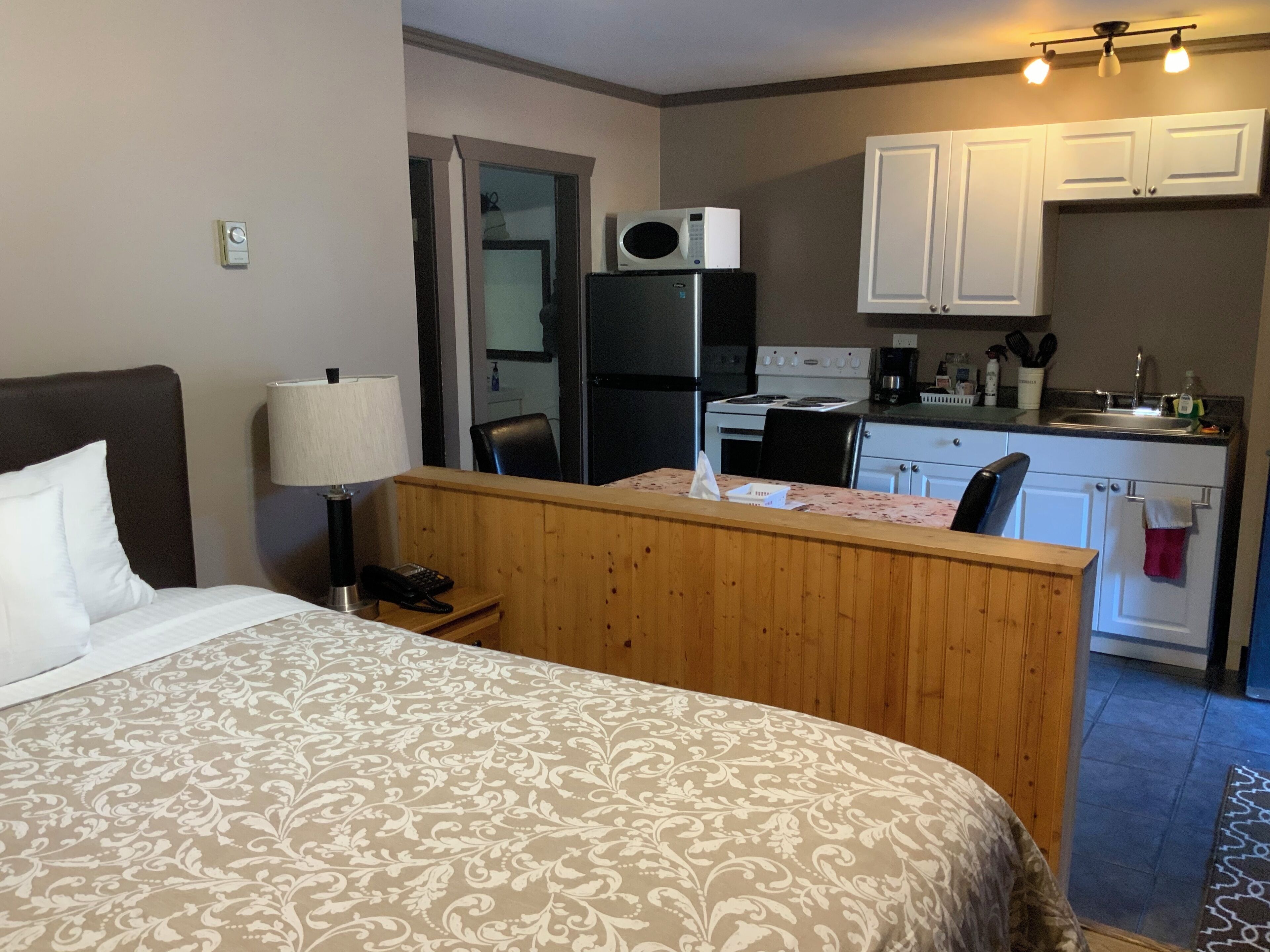 A hotel room with a bed, a desk, a kitchenette, and a bathroom.
