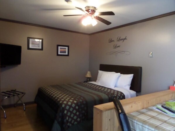 A hotel room with a bed, a ceiling fan, a wall-mounted TV, and a motivational quote on the wall. - Riverside Motel (Port Alberni)