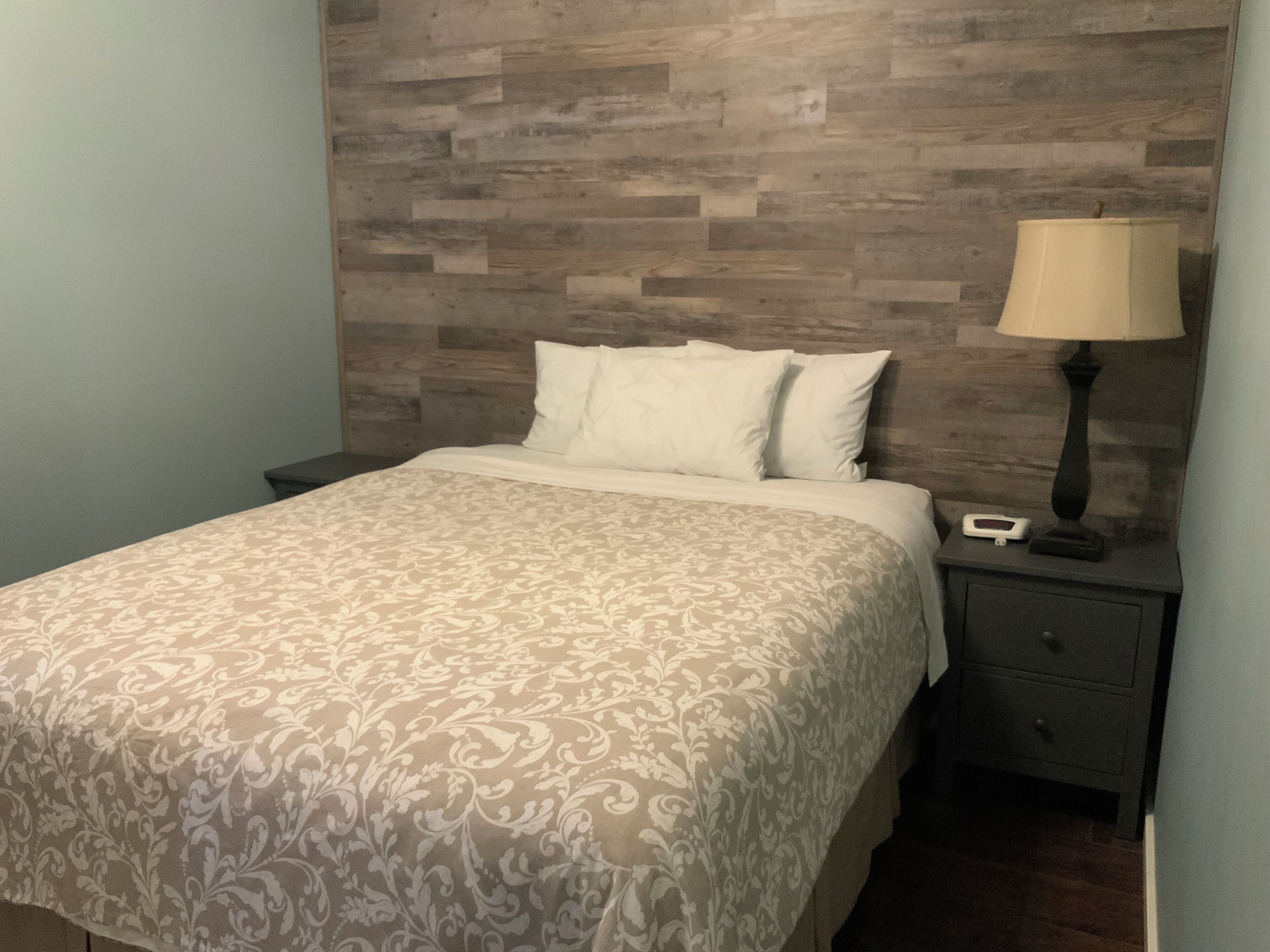 A neatly made bed with a patterned bedspread, a bedside lamp, and a nightstand with a small device.