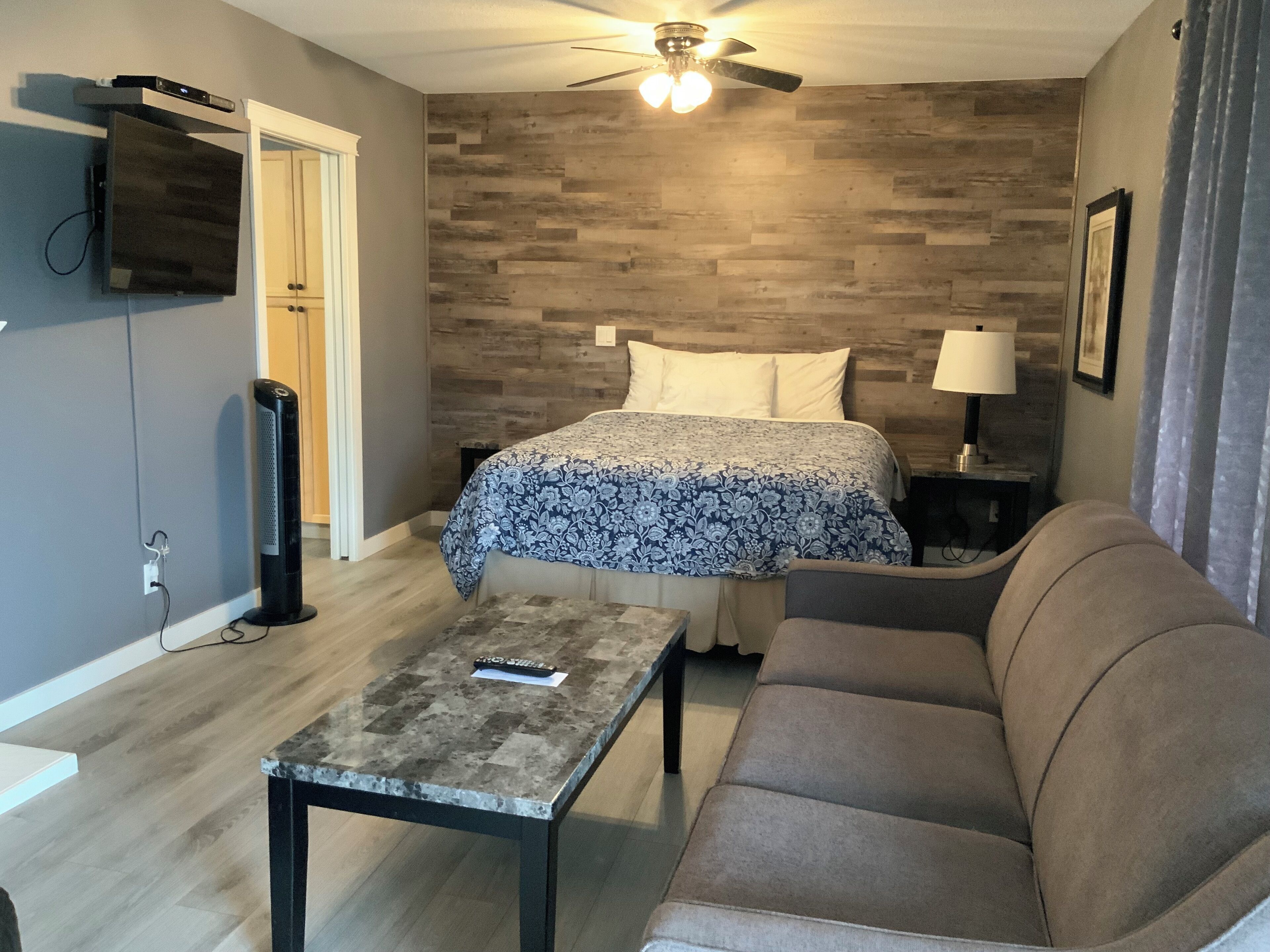A bedroom with a bed, a sofa, a table, a TV, and a ceiling fan.