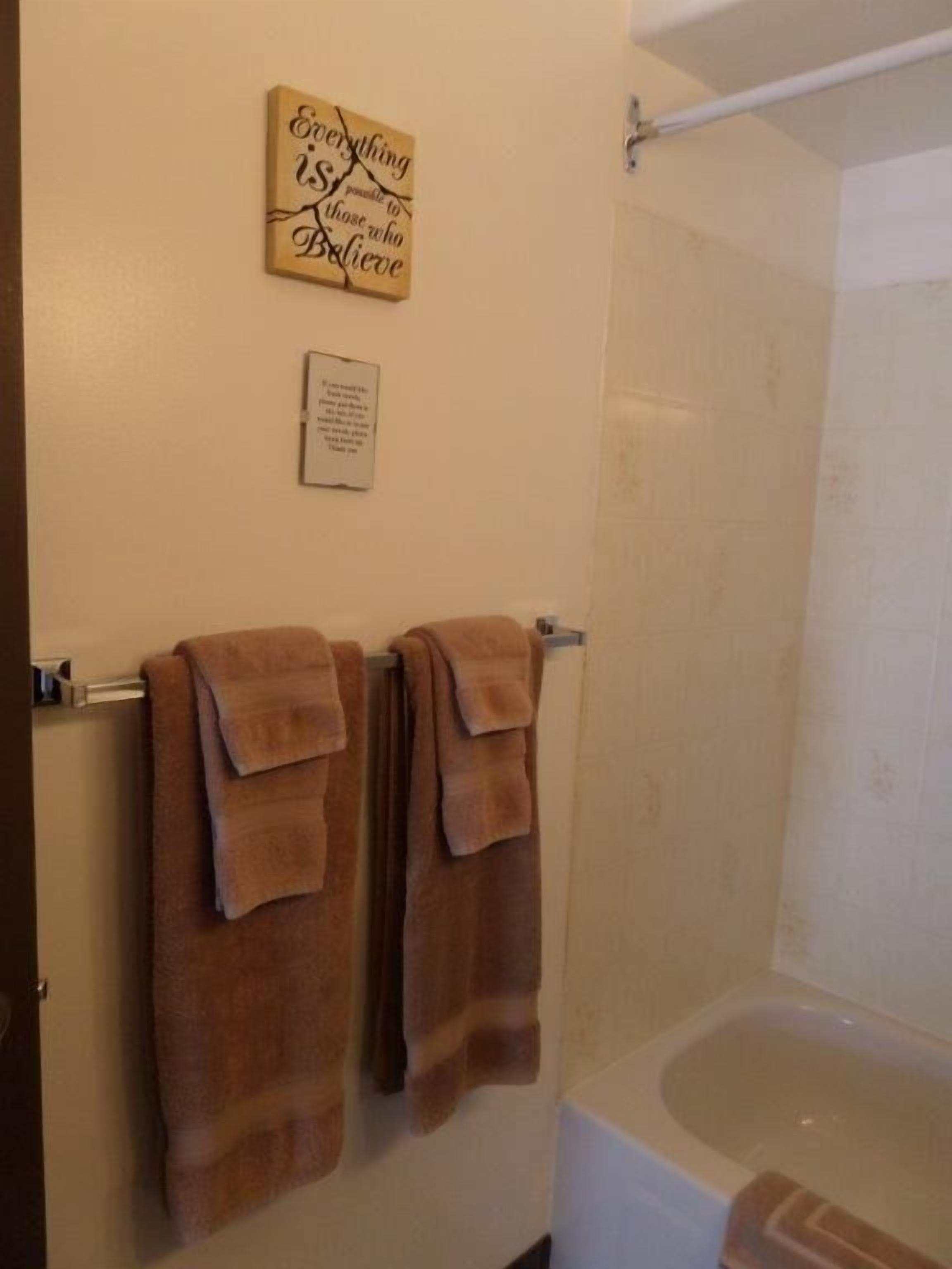 A bathroom with a bathtub, two towels hanging on a towel rack, and a motivational quote on the wall.