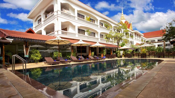 A hotel with a swimming pool, lounge chairs, umbrellas, and a traditional architectural style. - Lin Ratanak Angkor Hotel (Siem Reap)
