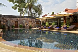 A swimming pool with lounge chairs and umbrellas, surrounded by stone walls and palm trees. - Lin Ratanak Angkor Hotel (Siem Reap)