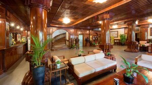 A spacious lobby with wooden flooring, a central seating area with a sofa and chairs, and multiple potted plants. - Lin Ratanak Angkor Hotel (Siem Reap)