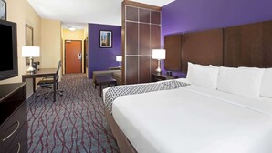 A hotel room with a large bed, a desk with a chair, a TV, and a bathroom door.