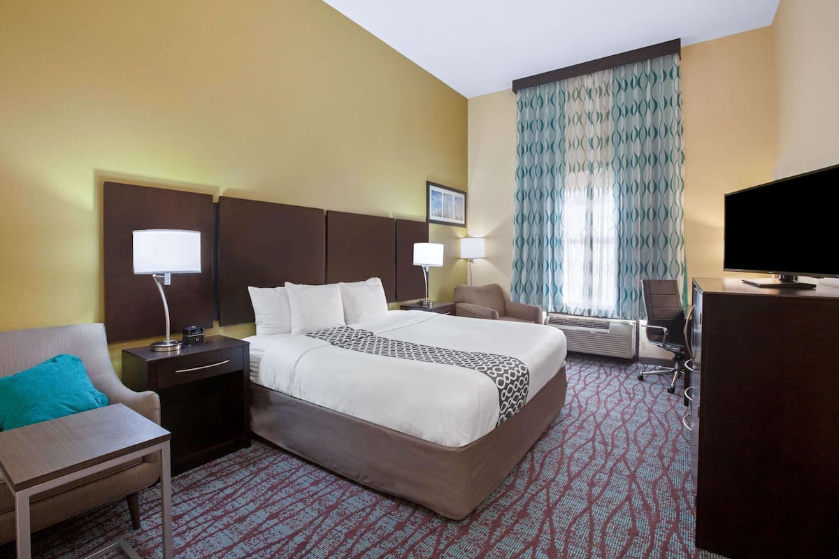 Una habitación de hotel con una cama grande, dos mesitas de noche con lámparas, un escritorio, una silla, un televisor y una alfombra estampada.