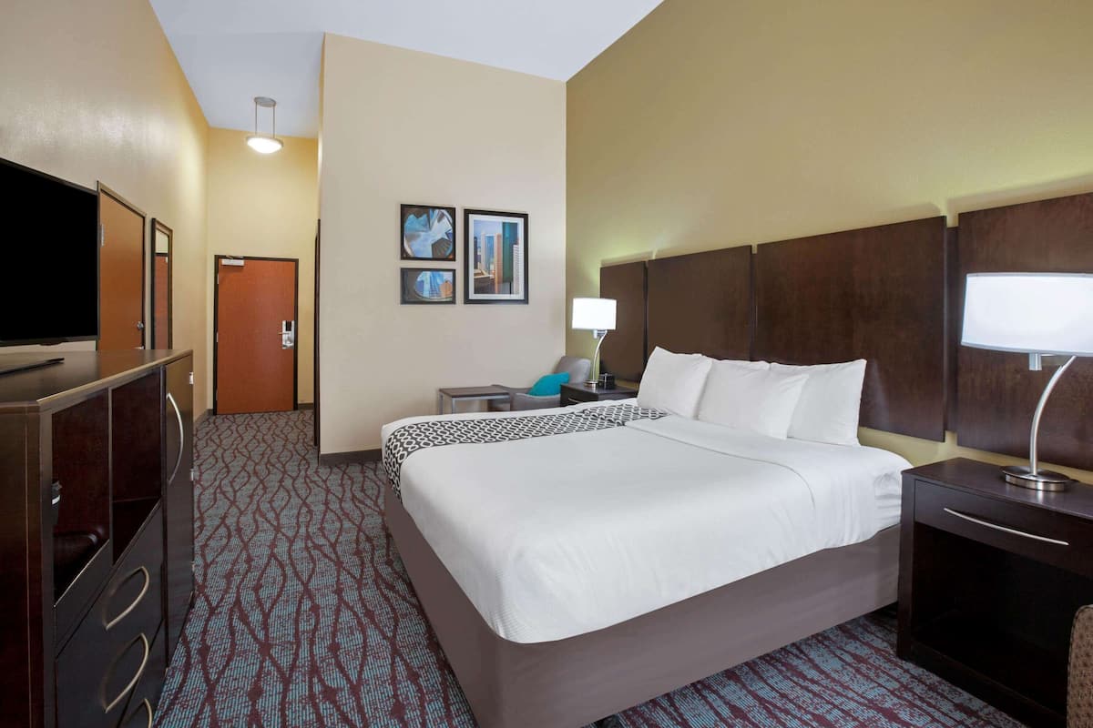 Habitación de hotel con una cama grande, televisión, escritorio con lámpara y una puerta.