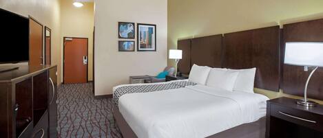 A hotel room with a large bed, a TV, a desk with a lamp, and a door.