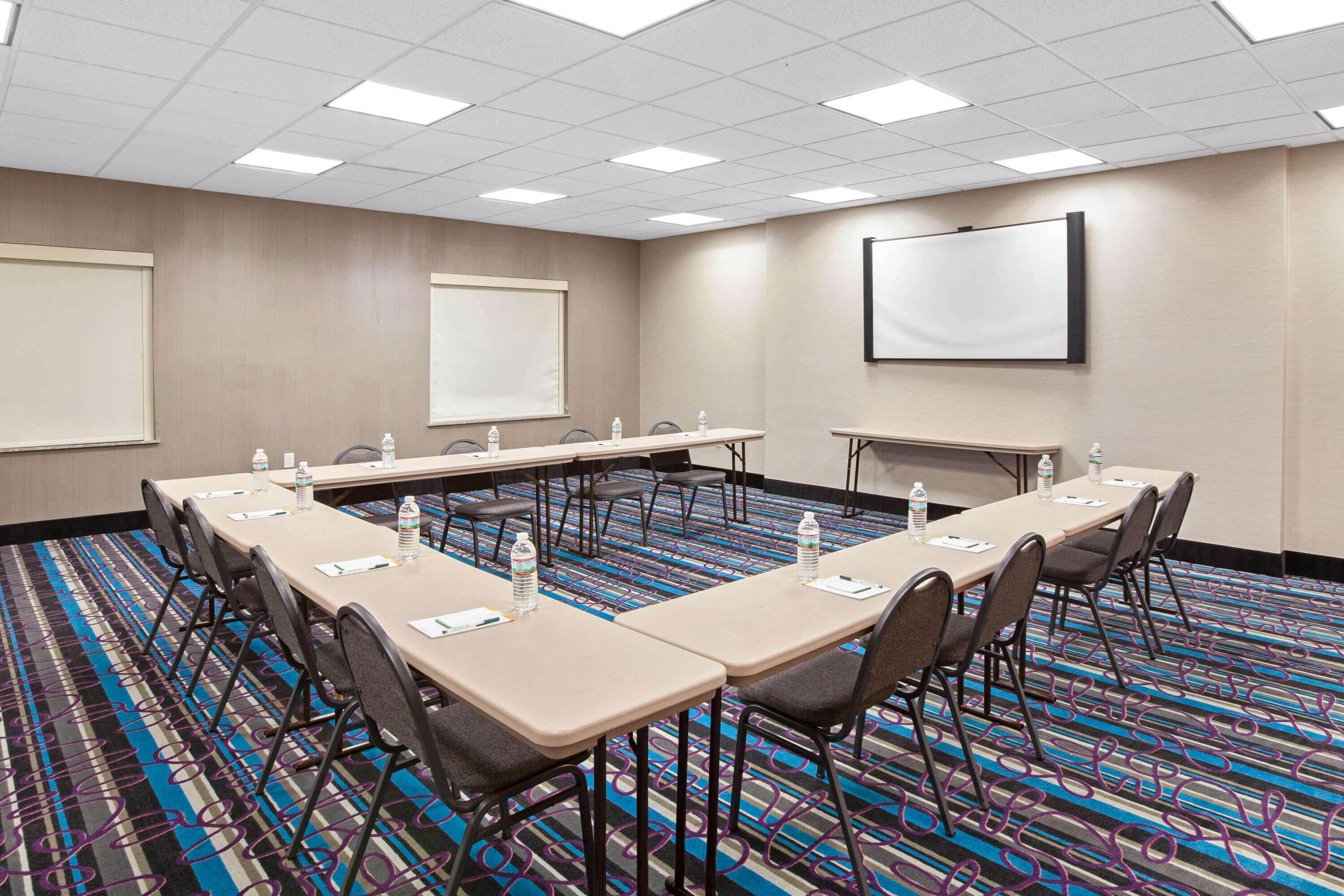 A conference room with a long table, chairs, a projector screen, and a carpeted floor.