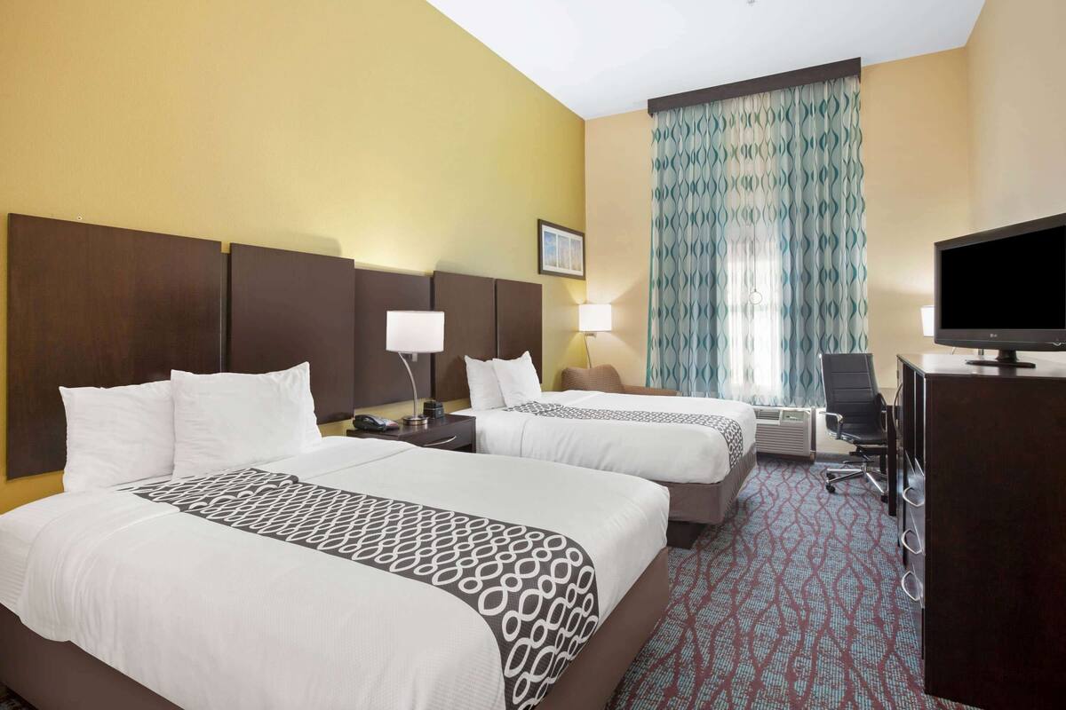 Habitación de hotel con dos camas, un escritorio, un televisor y una ventana con cortinas estampadas.