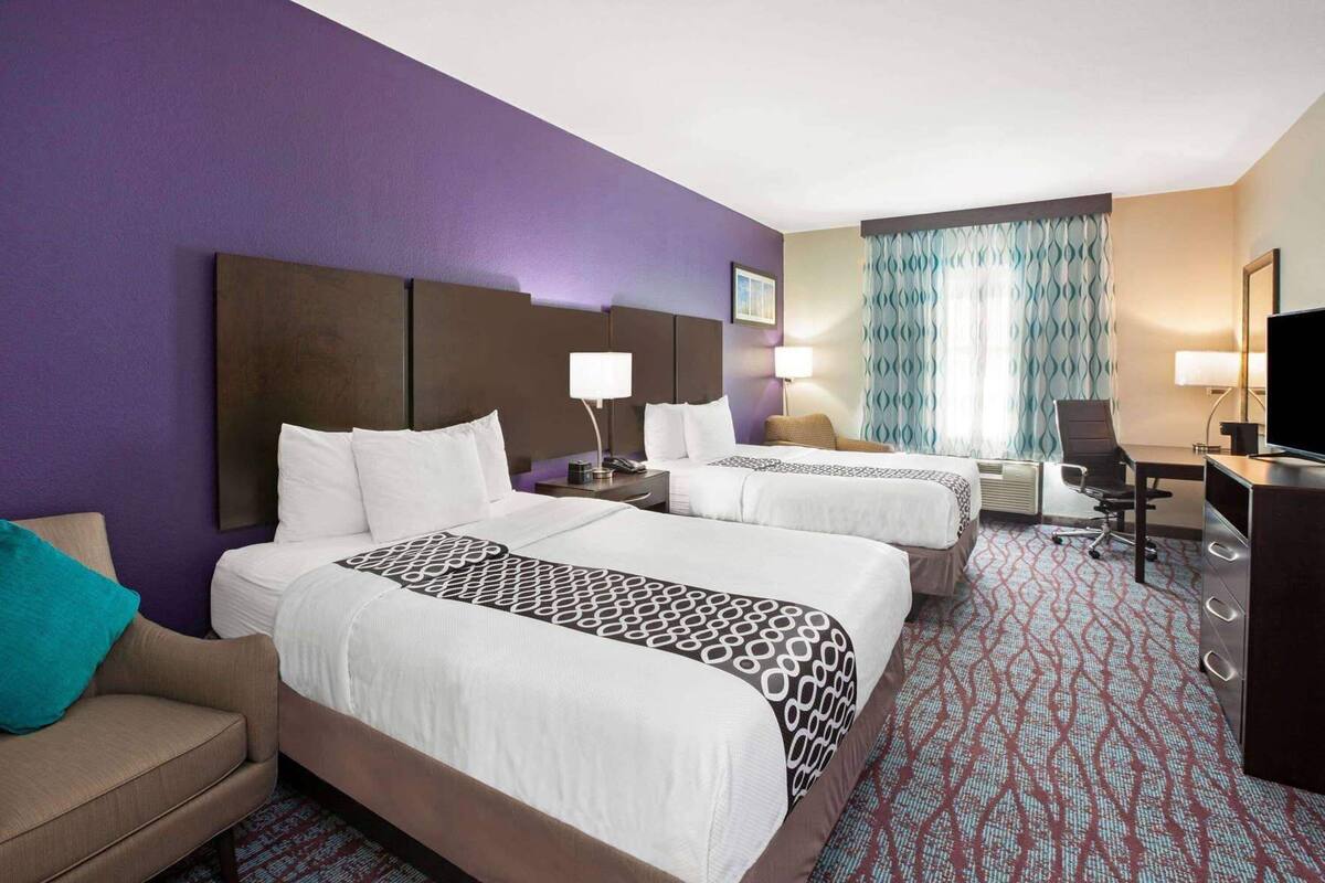 A hotel room with two beds, a desk, a chair, a TV, and a window with curtains.