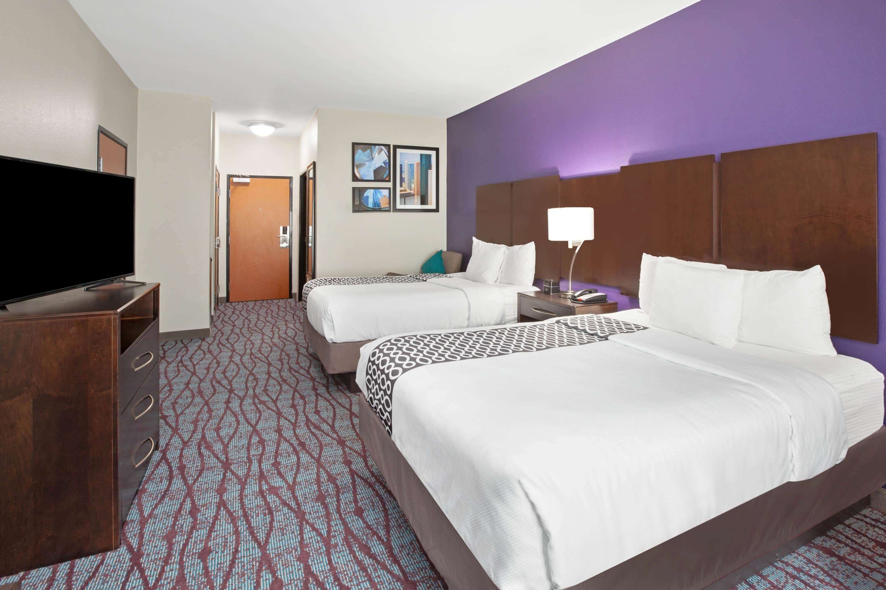 A hotel room with two beds, a TV, a desk, and a bathroom door.