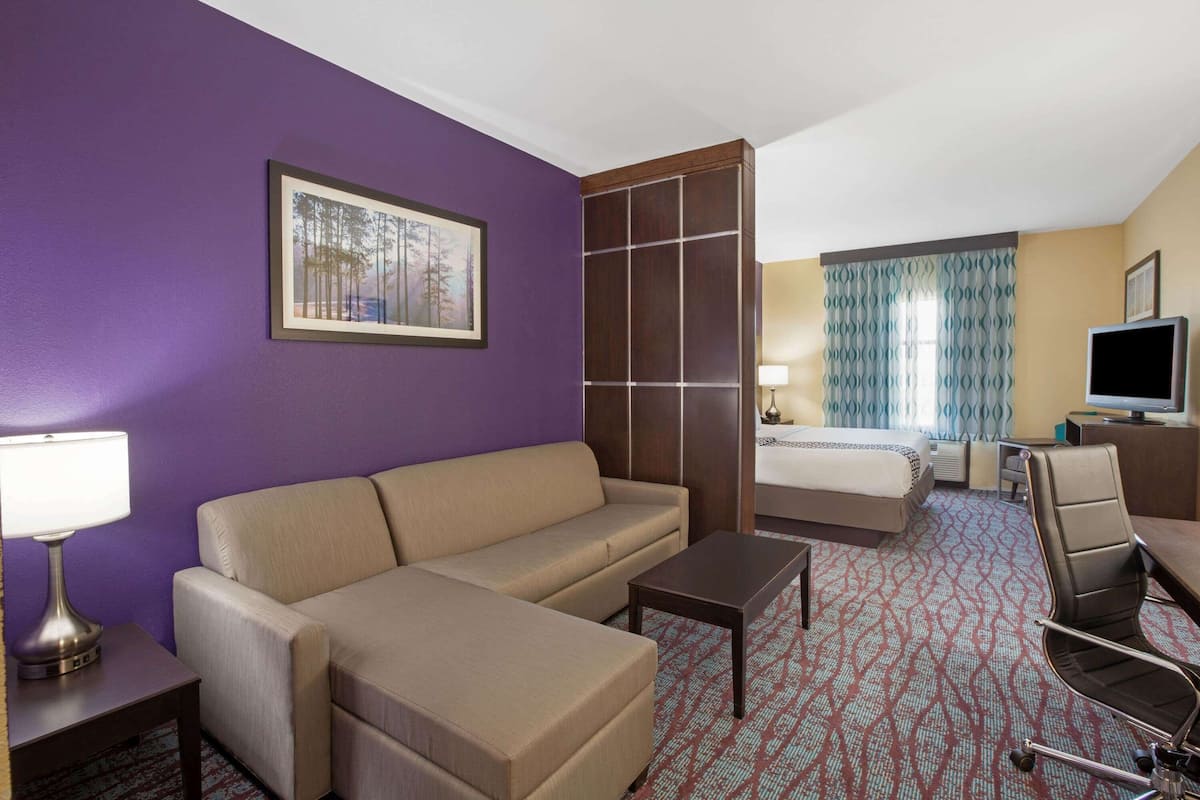 Habitación de hotel con sofá, una mesita, televisor, cama y ventana con cortinas.