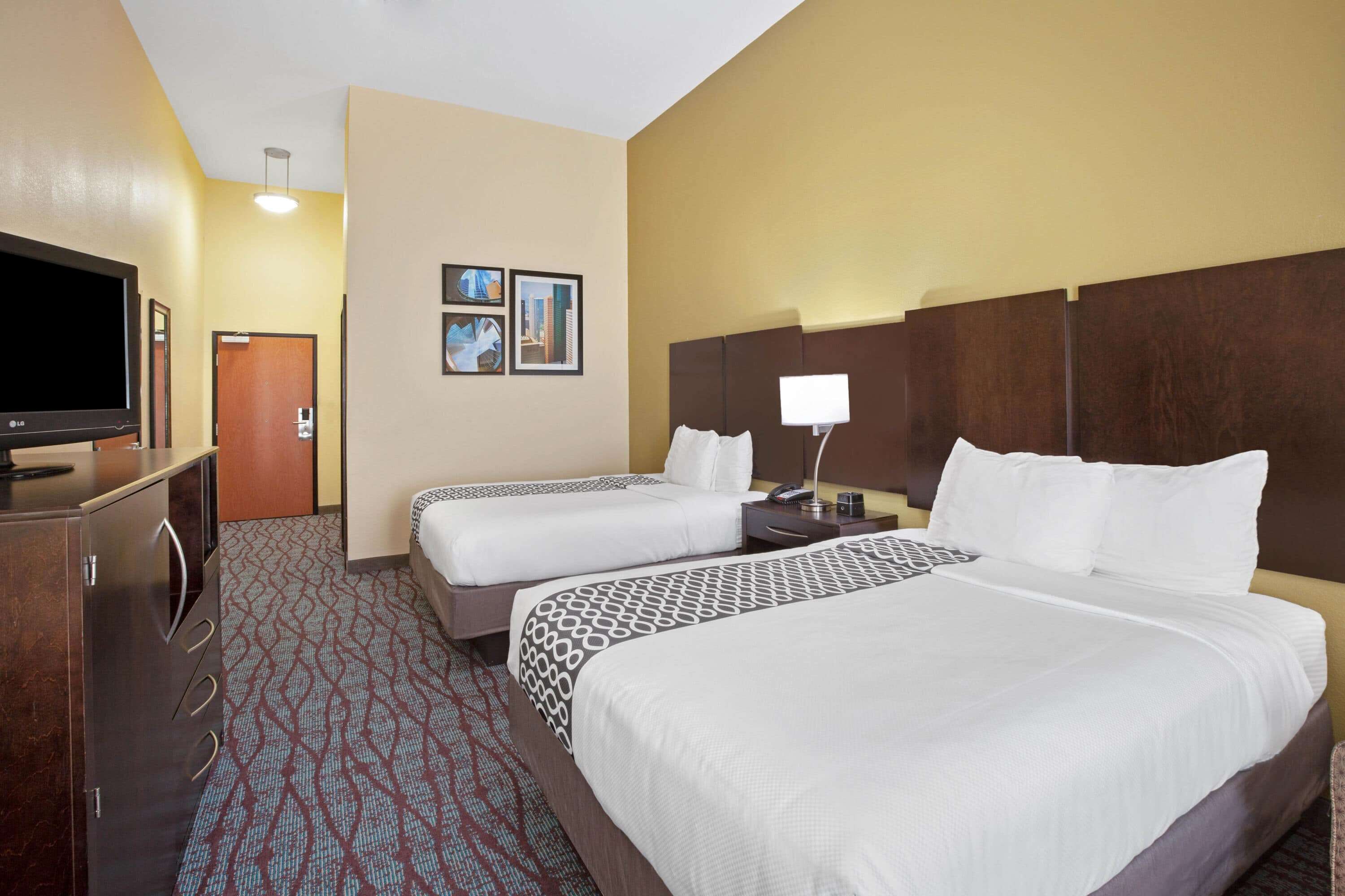 A hotel room with two beds, a TV, a desk, and a lamp.