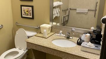 A bathroom with a toilet, sink, and shower. There are framed pictures on the wall, a towel rack, and a coffee machine.