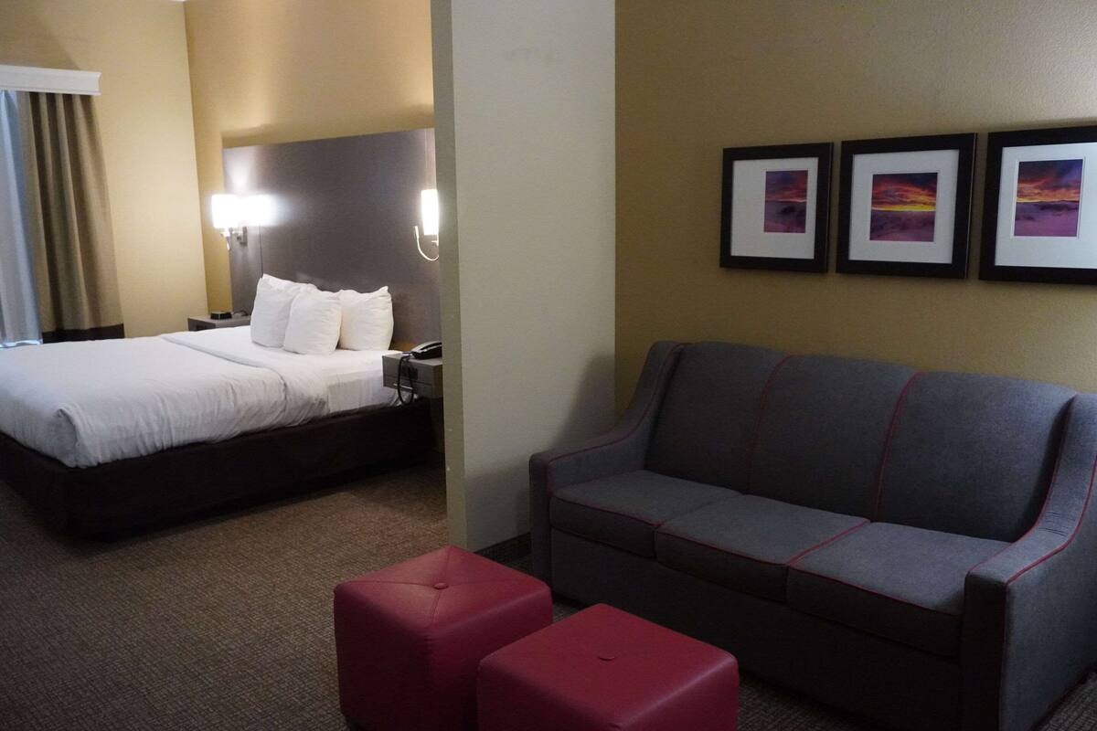 A hotel room with a bed, a sofa, and three framed pictures on the wall.