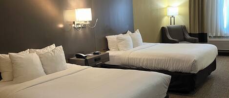 A hotel room with two beds, a desk, a chair, and a window with curtains.