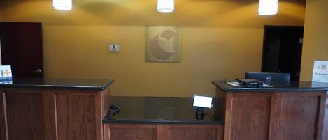 A reception desk with wooden paneling and a glass partition, overhead pendant lighting, and a wall-mounted sign.