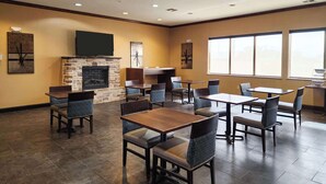 A spacious indoor dining area with multiple tables and chairs, a stone fireplace, and large windows allowing natural light. - Comfort Inn & Suites Monahans I-20 (Monahans)
