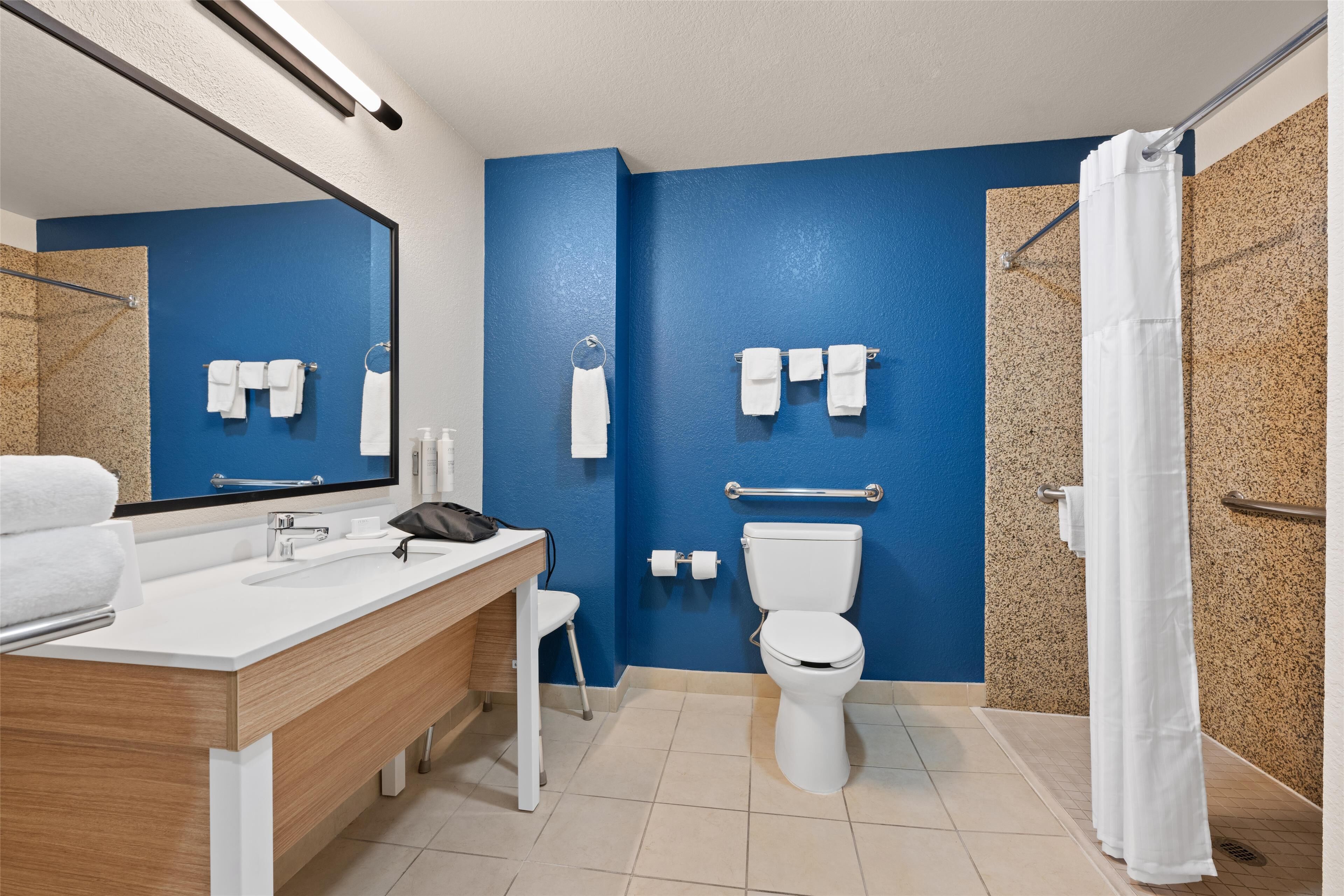 A modern bathroom with a blue accent wall, a white sink, a toilet, and a shower area.