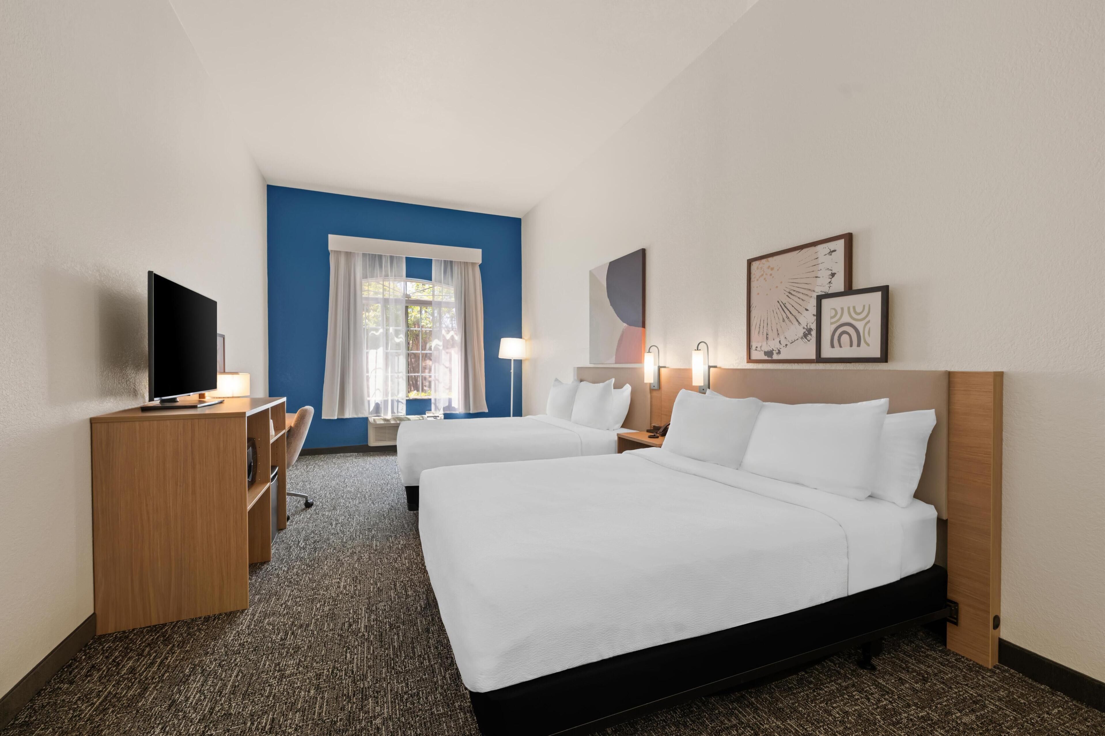 Una habitación de hotel con dos camas, un escritorio, un televisor y una ventana con cortinas.