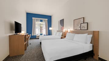 A hotel room with two beds, a desk, a TV, and a window with curtains.