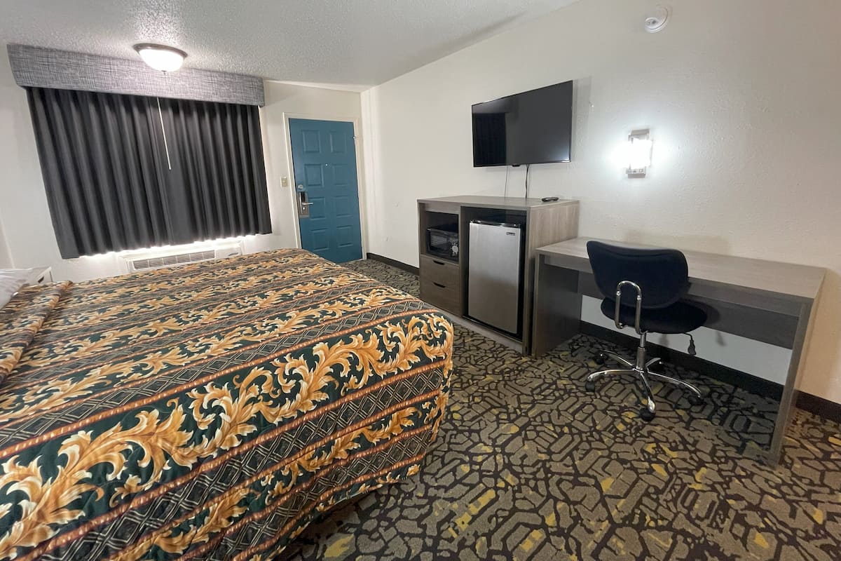 A hotel room with a bed, a desk, a chair, a television, and a door.