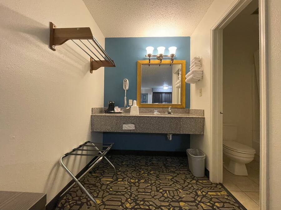 Une salle de bain dotée d’un comptoir en granit, d’un miroir avec éclairage intégré, d’un porte-serviettes, d’une poubelle et d’un carrelage décoratif.