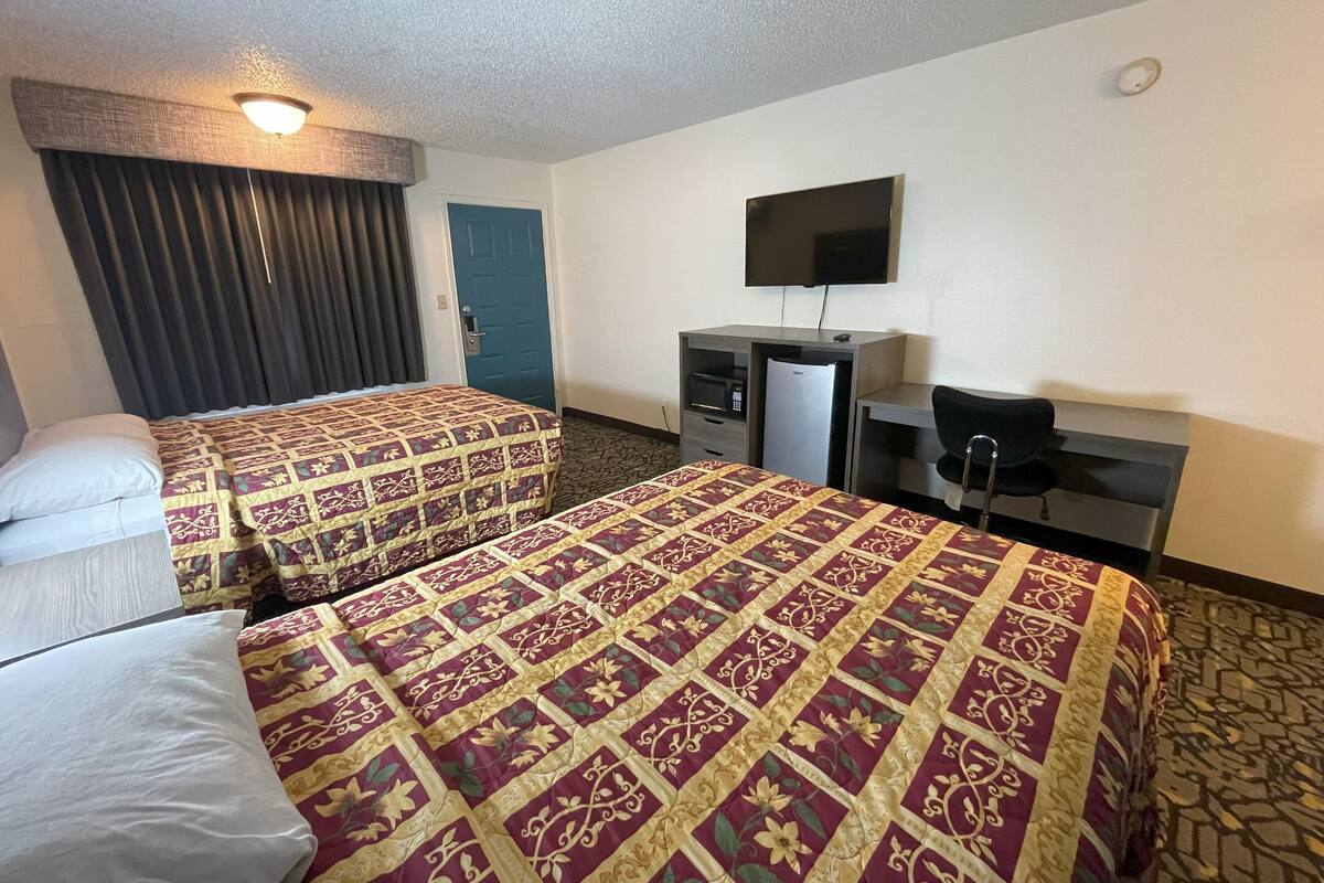 A hotel room with two beds, a desk, a chair, a television, and a refrigerator.