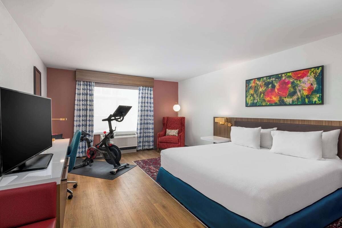 Habitación de hotel con cama, escritorio con televisor, bicicleta estática y una silla roja.