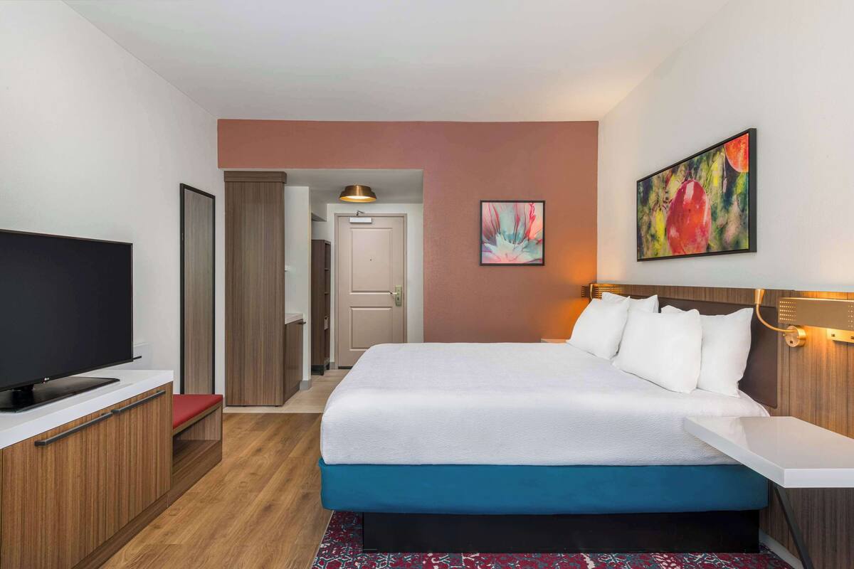 Una habitación de hotel con cama, televisión, escritorio y puerta que da a un pasillo.