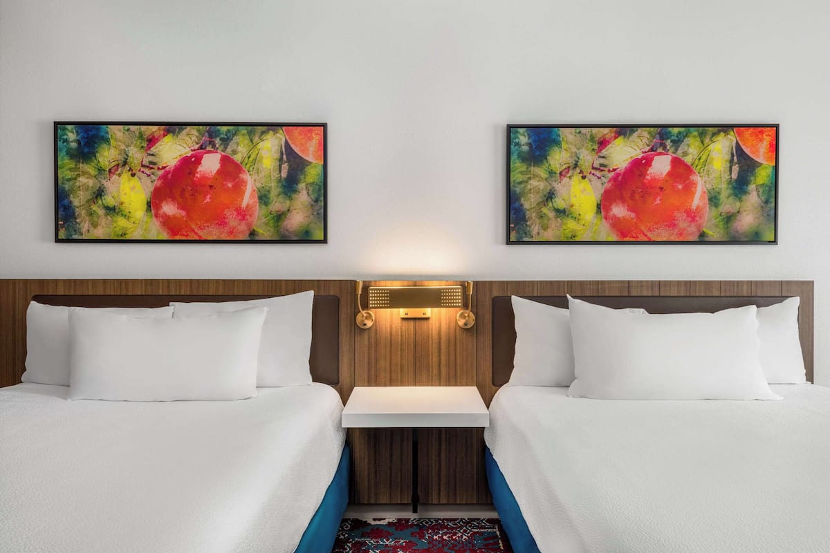 Una habitación de hotel con dos camas, una mesita y dos cuadros en la pared.