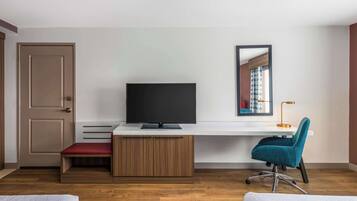 A modern room with a wooden floor, a desk with a flat-screen TV, a teal office chair, a red bench, and a door.
