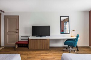 A modern room with a wooden floor, a desk with a flat-screen TV, a teal office chair, a red bench, and a door.
