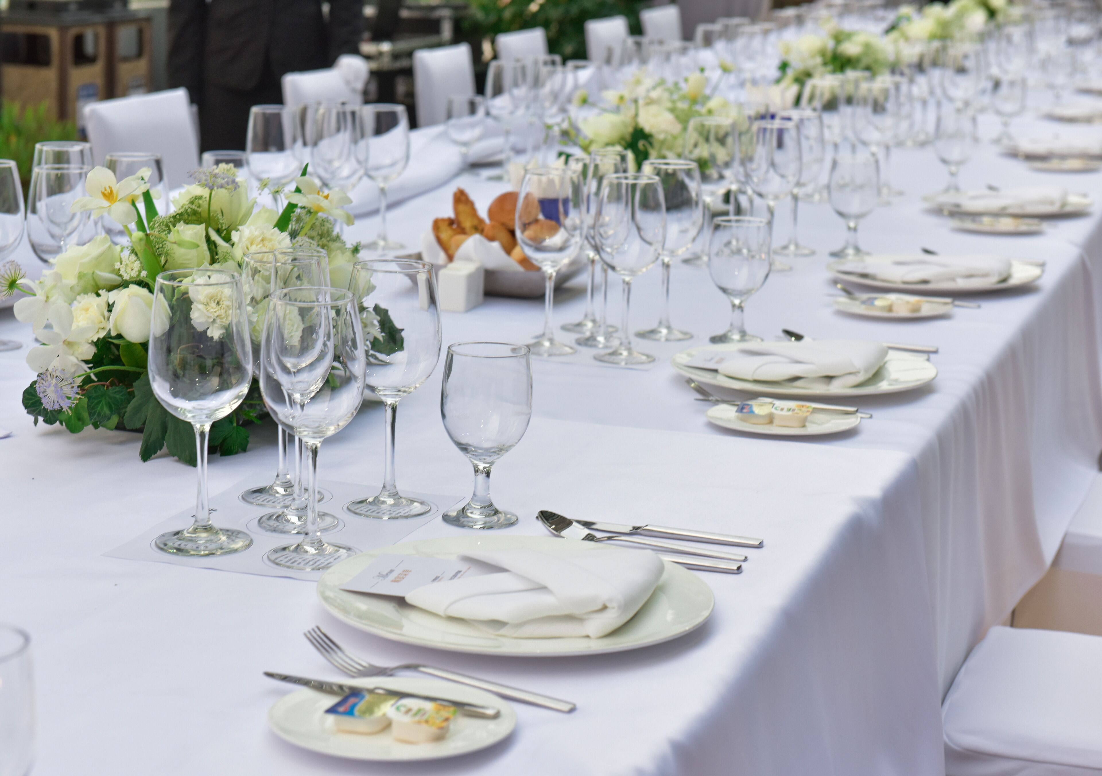 A long dining table set for a formal event with white tablecloths, glassware, and floral centerpieces.